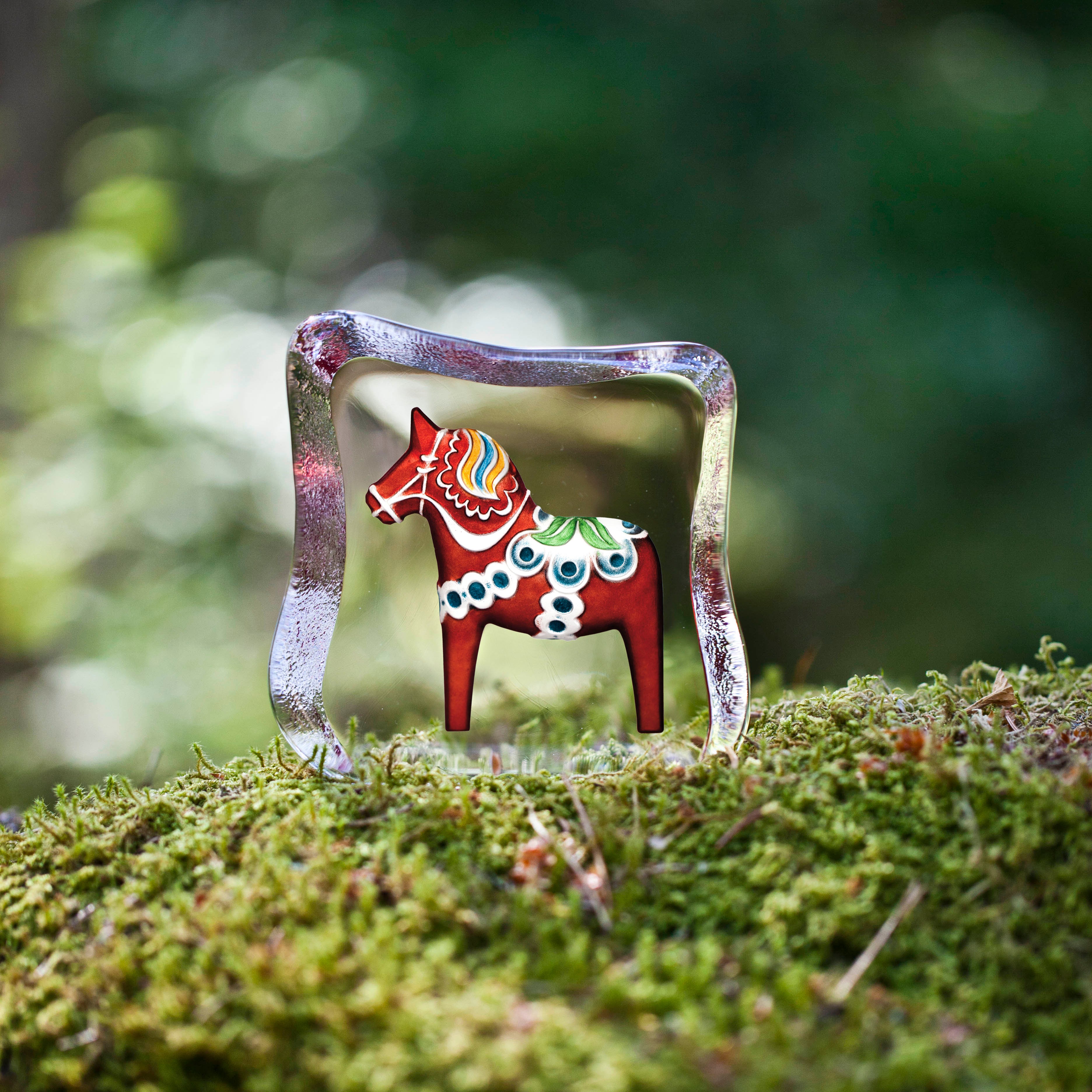 Decorative horse figurine with a glass base on a mossy surface
