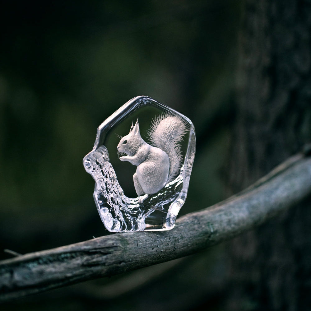 Crystal sculpture of a squirrel on a branch with a dark forest background