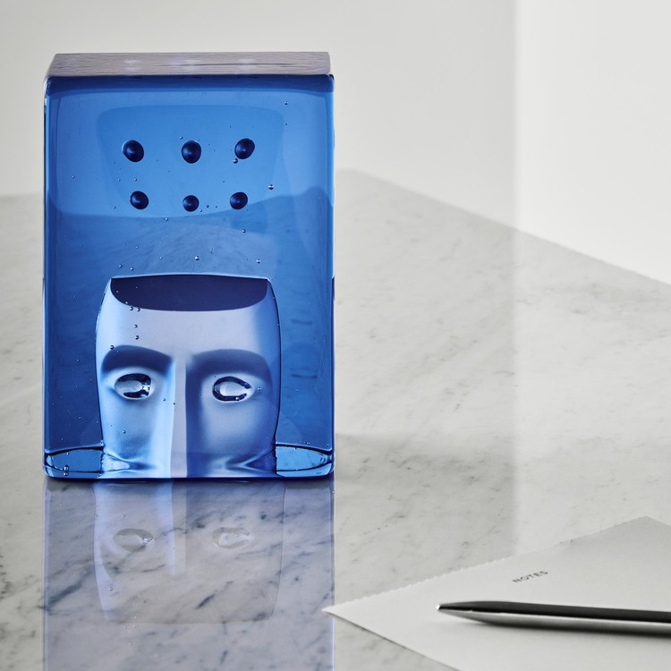 Azur blue glass object with a face design on a glass surface