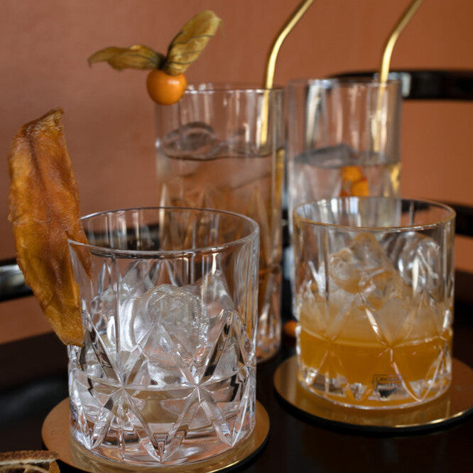 Cocktails with garnishes and straws on a dark surface with a warm background