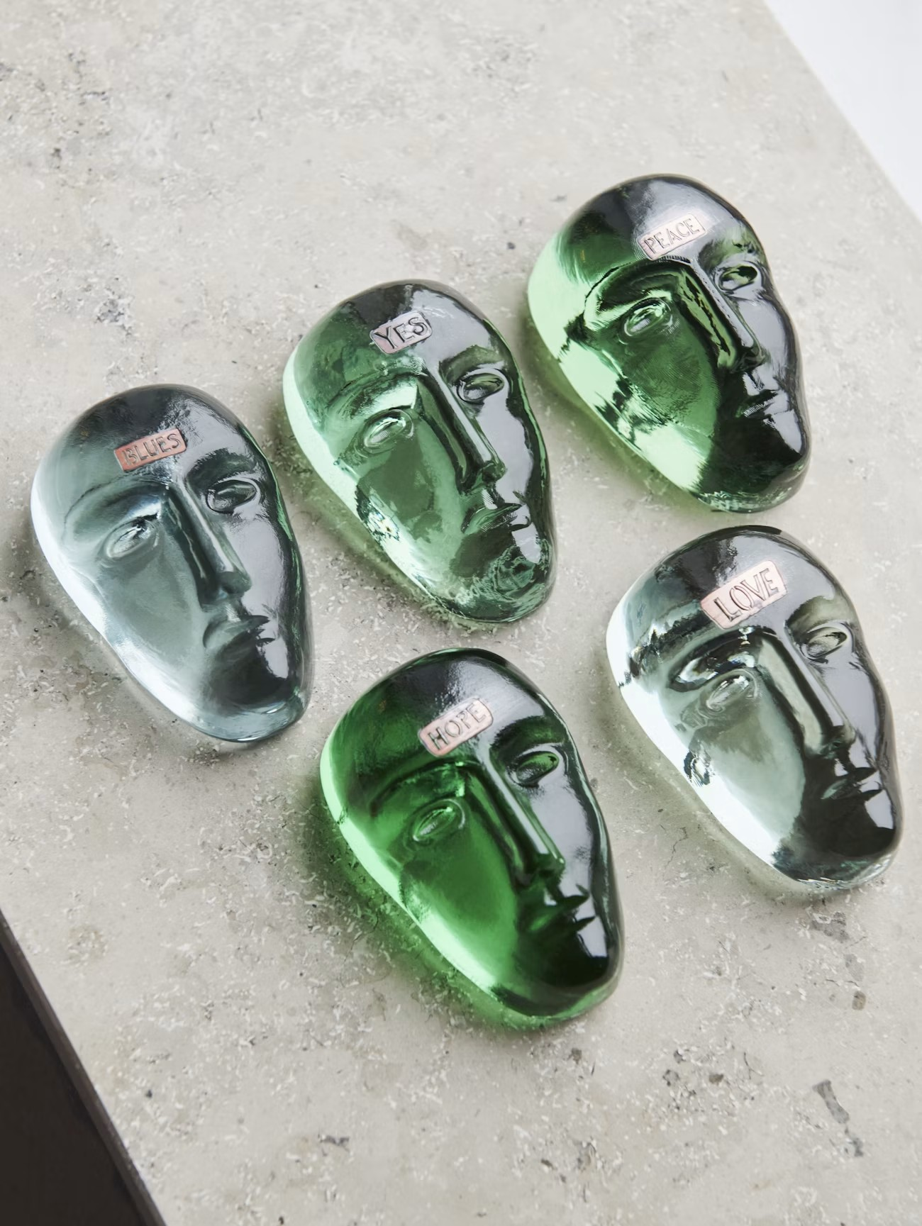 Kosta Boda green glass face sculptures on a concrete surface
