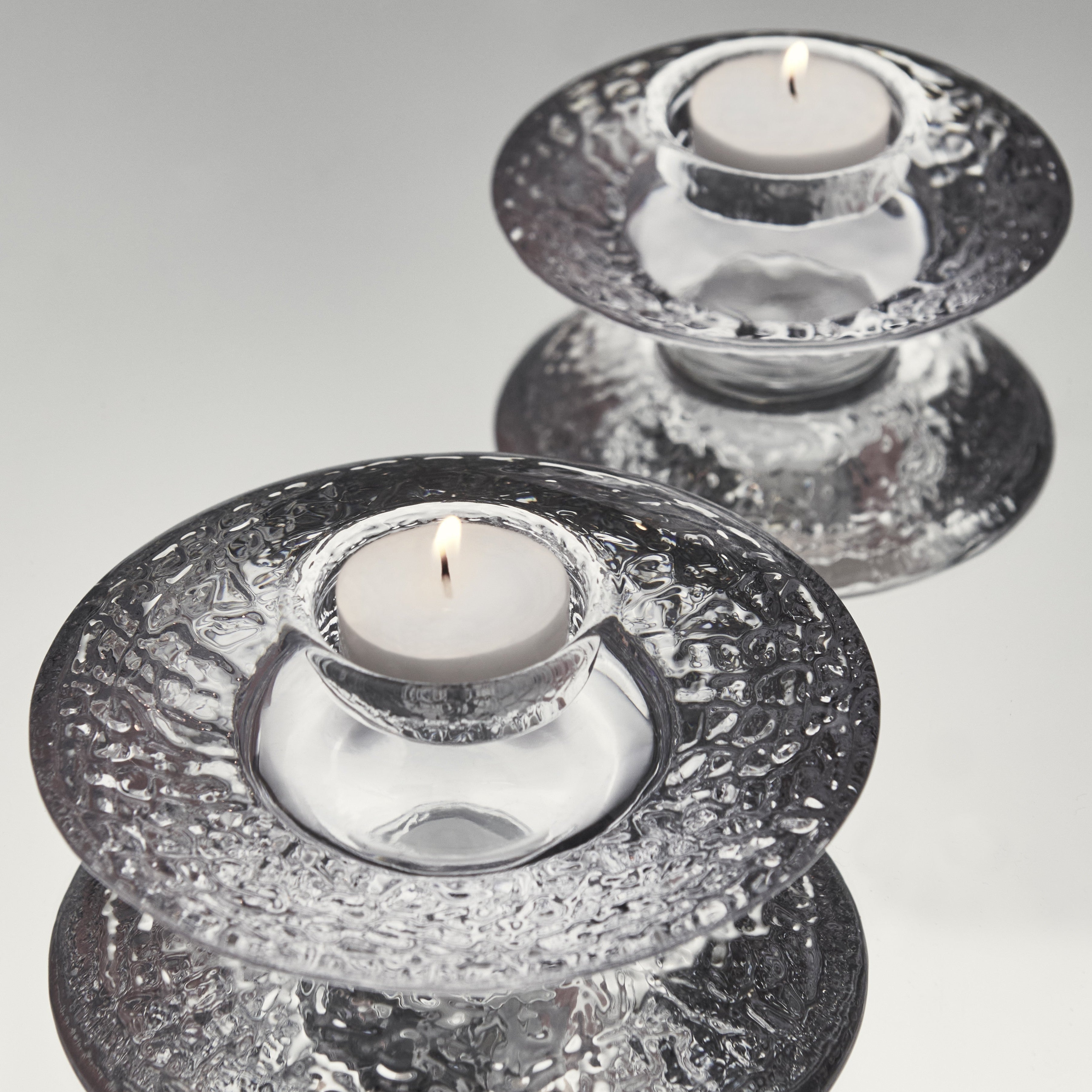 Two Orrefors crystal candle holders with candles on a reflective surface