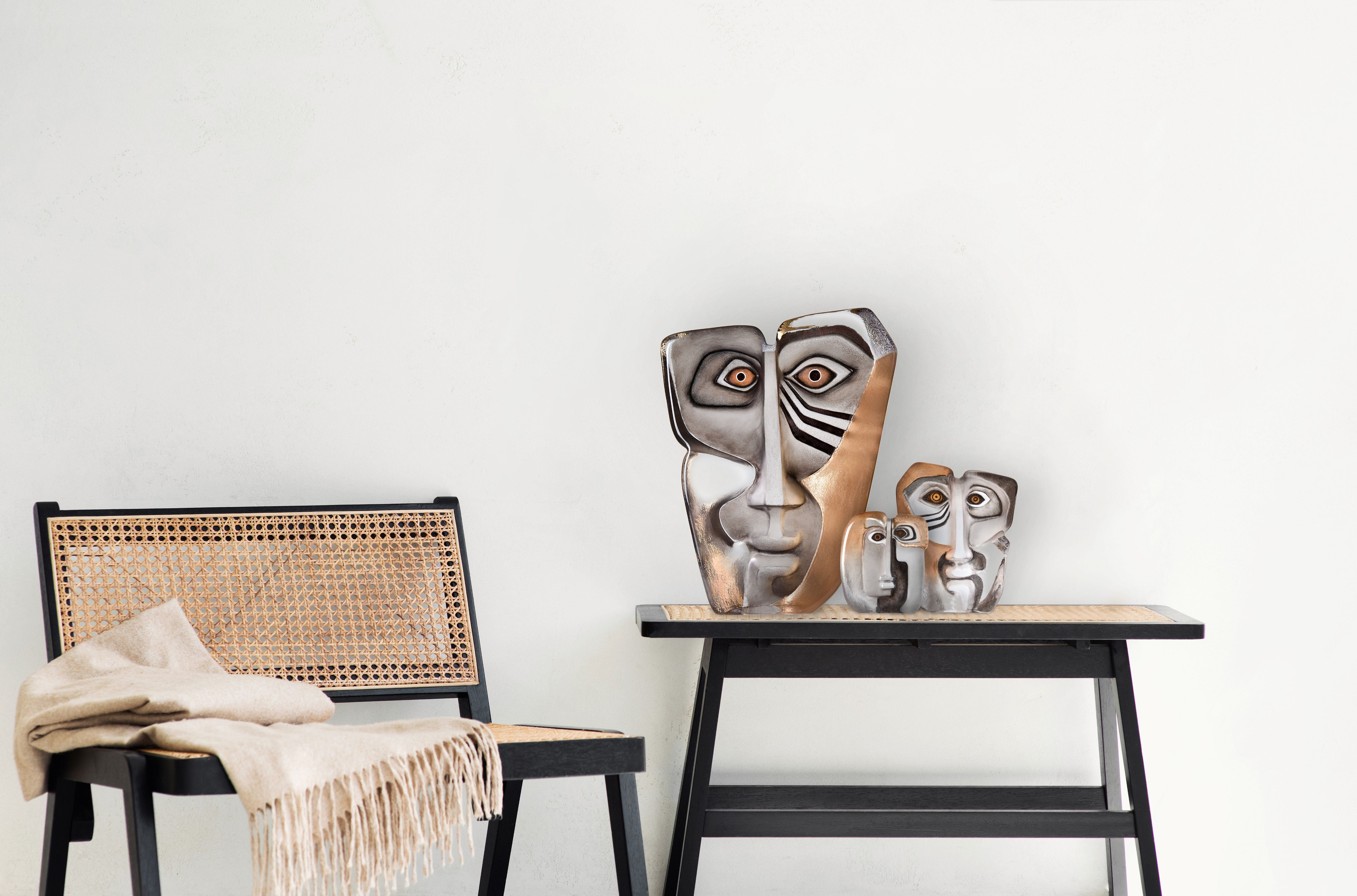 Glass masks sculptures and a wicker chair against a white wall
