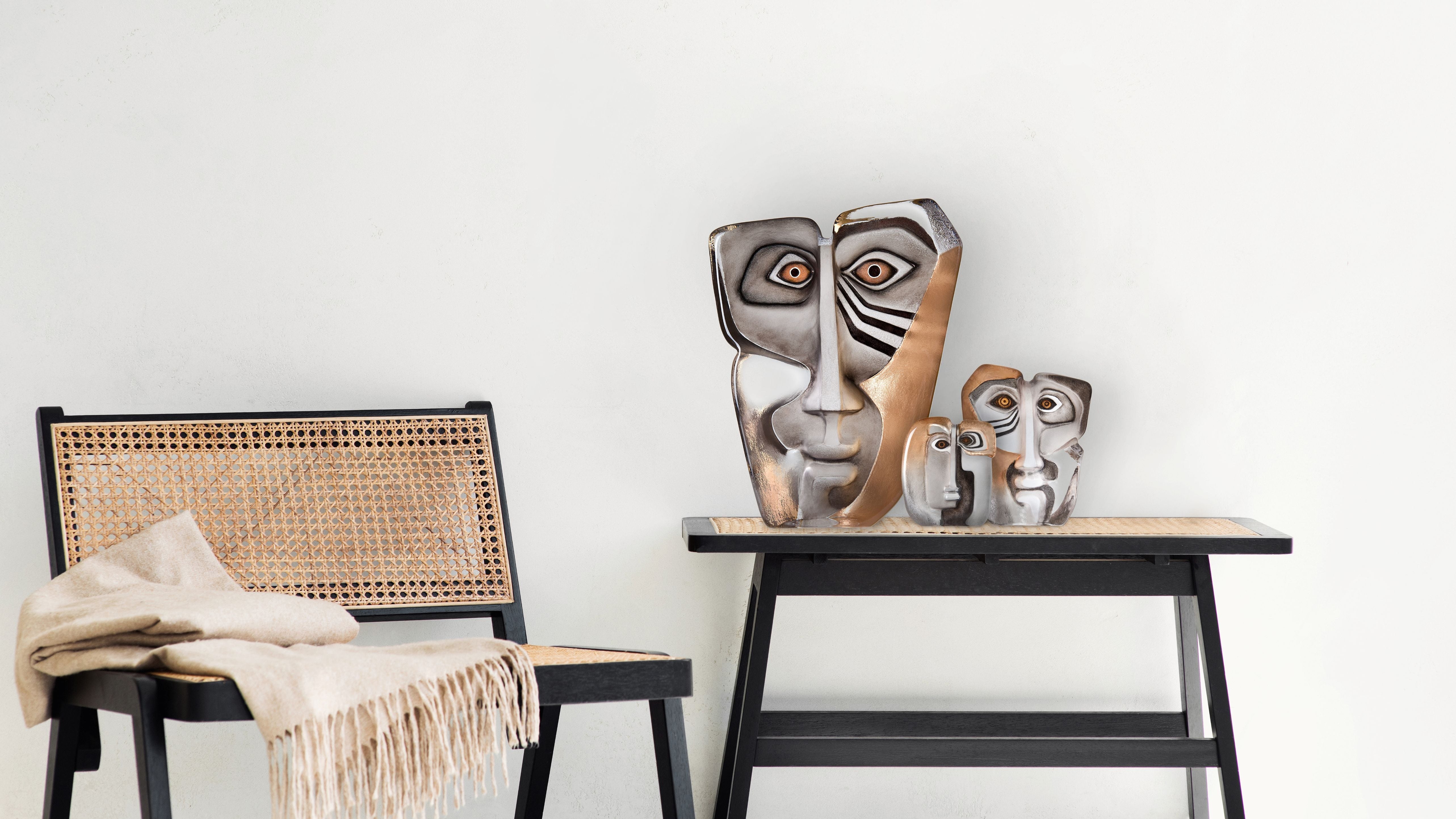 Maleras Glass masks sculptures and a wicker chair against a white wall