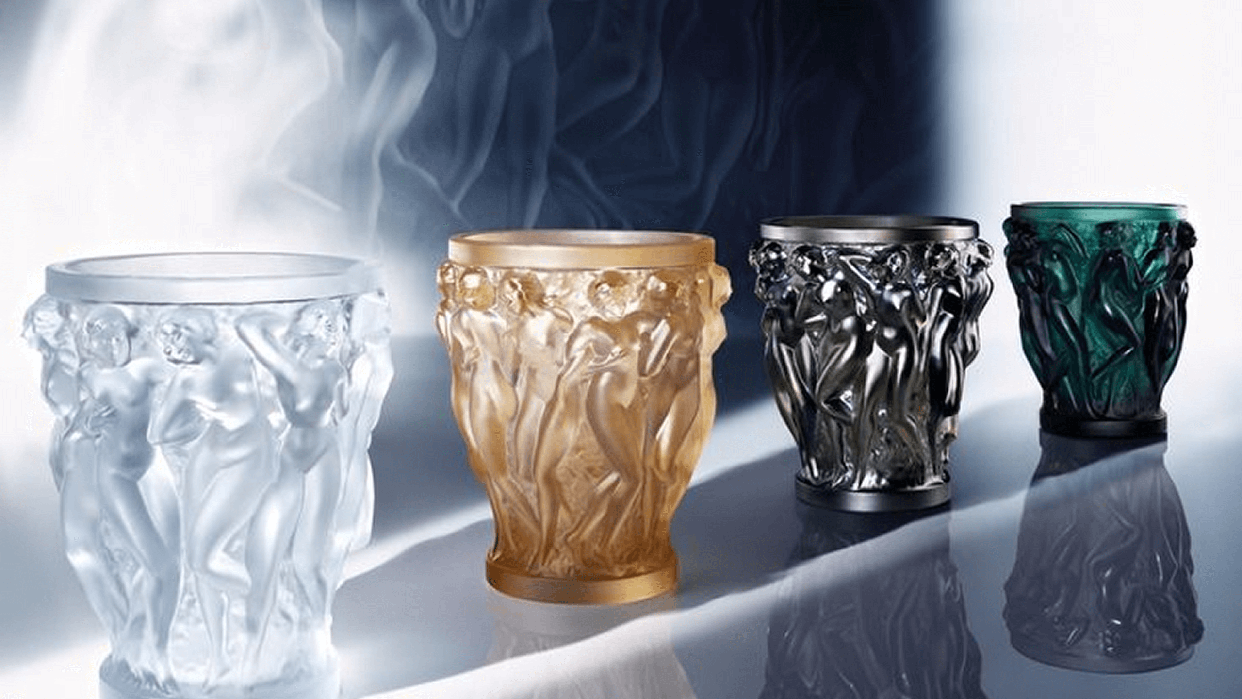 Set of four Lalique decorative vases with intricate designs on a reflective surface.