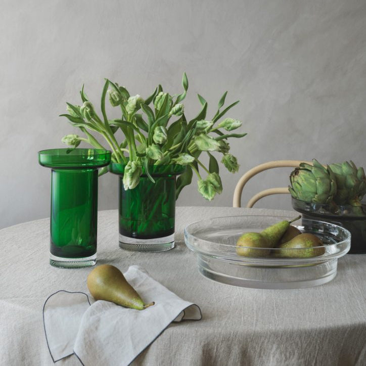 Table setting with Kosta Boda green Limelight glasses, a vase of flowers, and pears on a neutral background