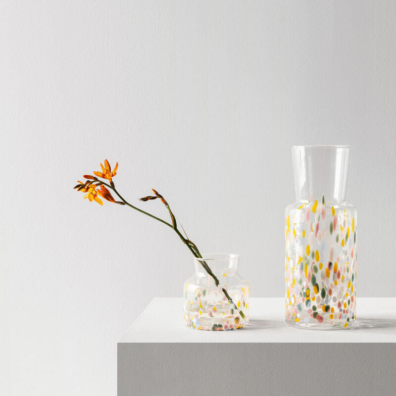 Two glass Kosta Boda Meadow vases with floral patterns on a white surface against a light grey background