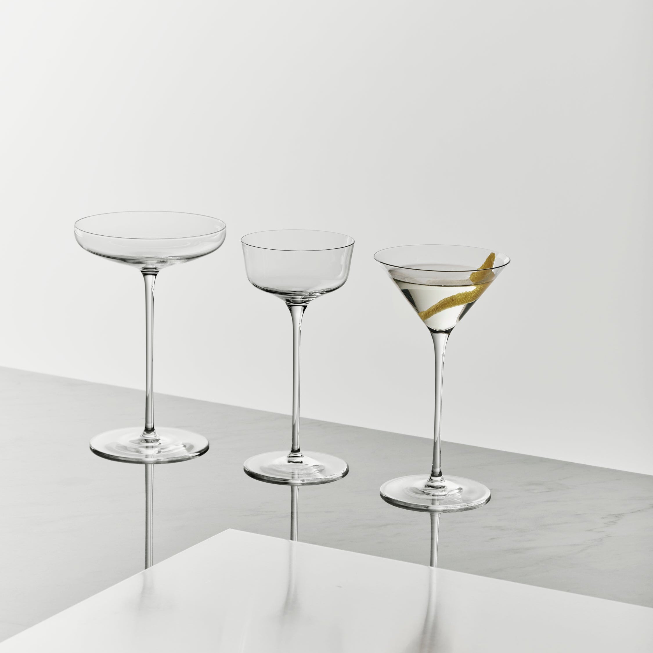 Three glass cocktail glasses on a reflective surface with a light gray background