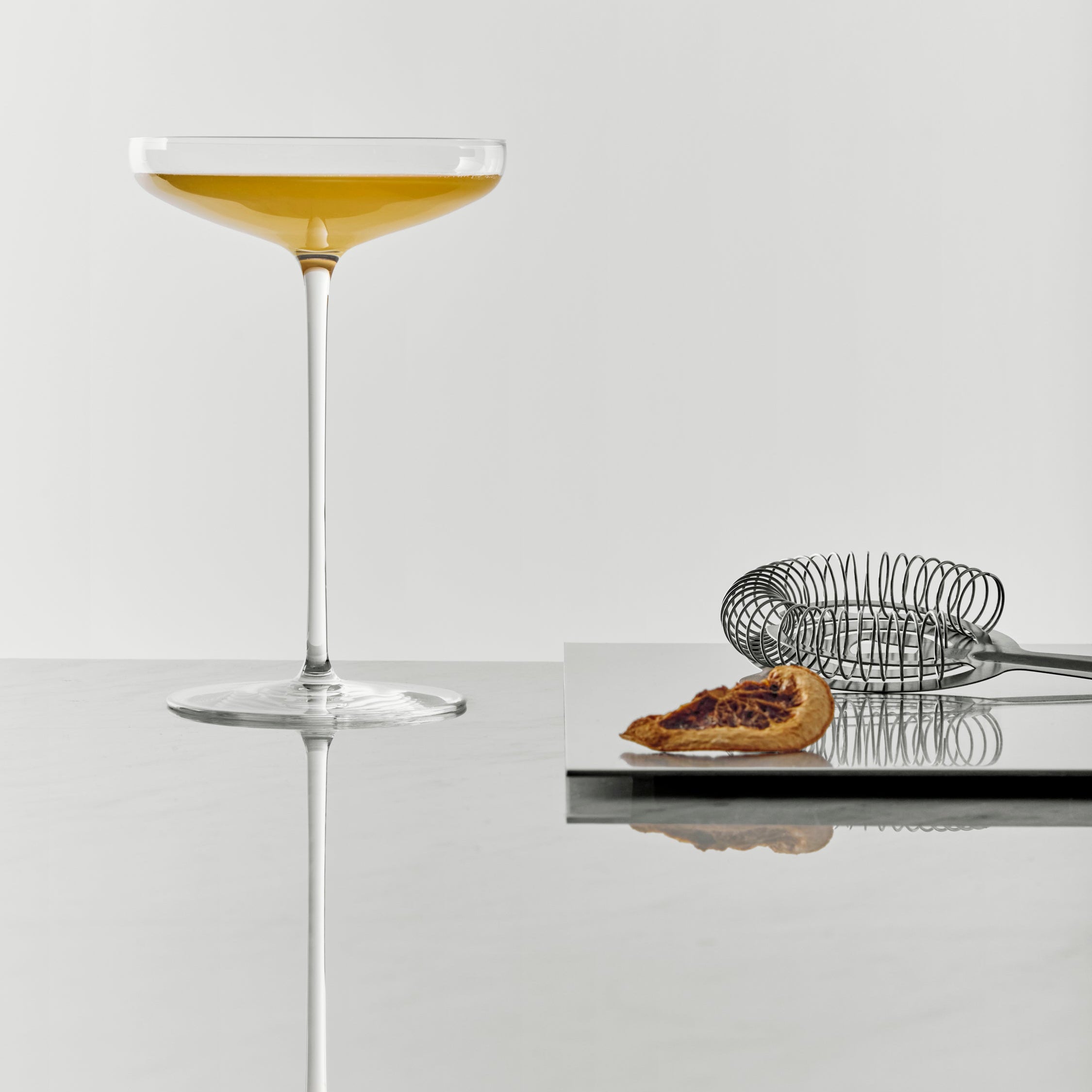 Frantzen Cocktail glass with a drink on a reflective surface with a blurred background