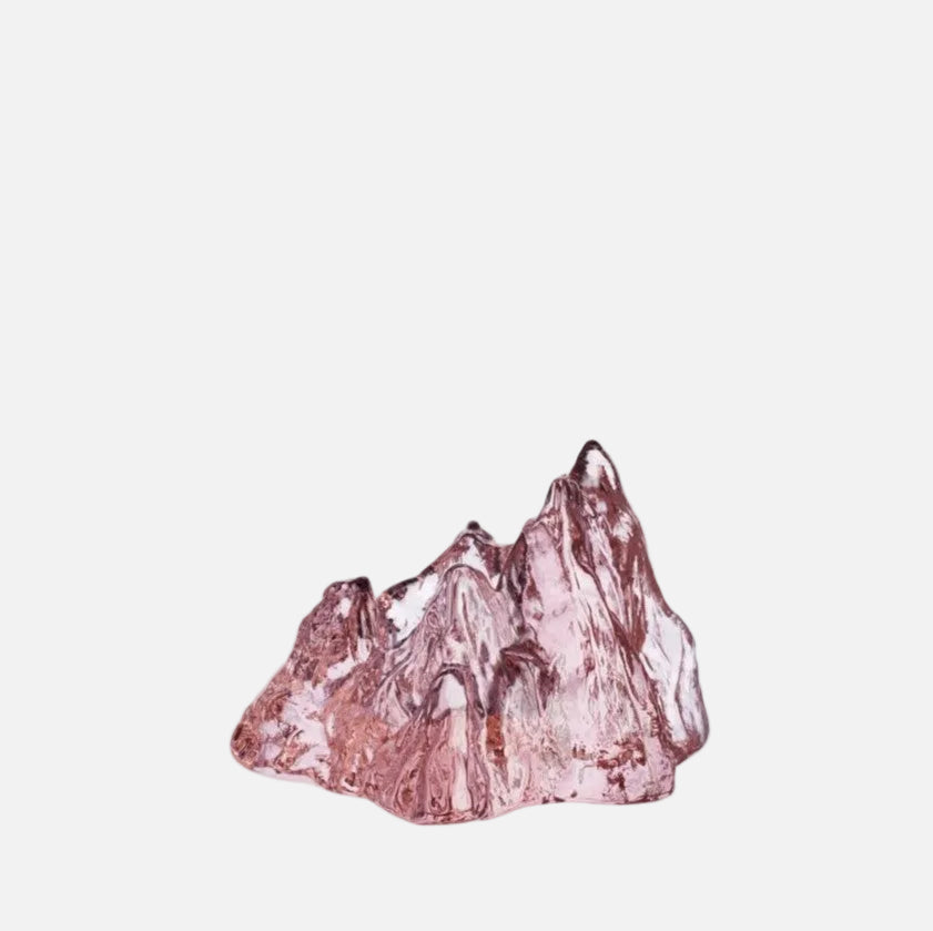 A pink circular glass votive with an irregular, rocky silhouette