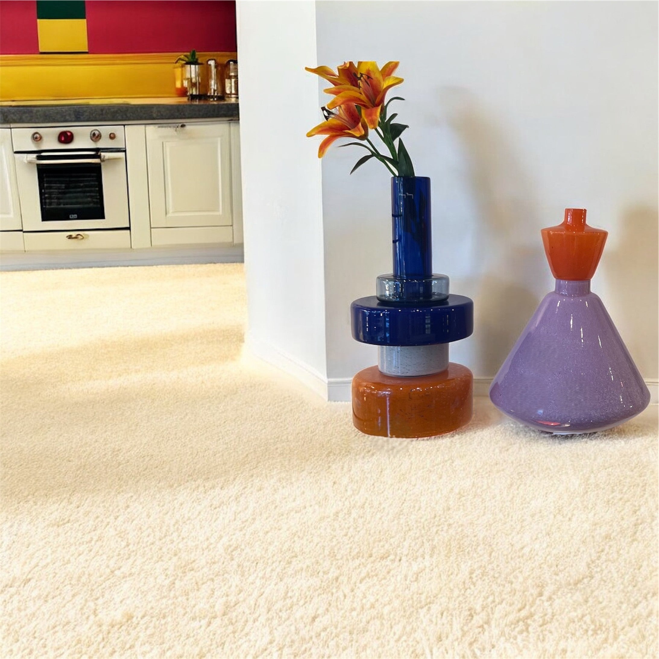 Colorful glass sculptures on a carpeted floor with a kitchen in the background