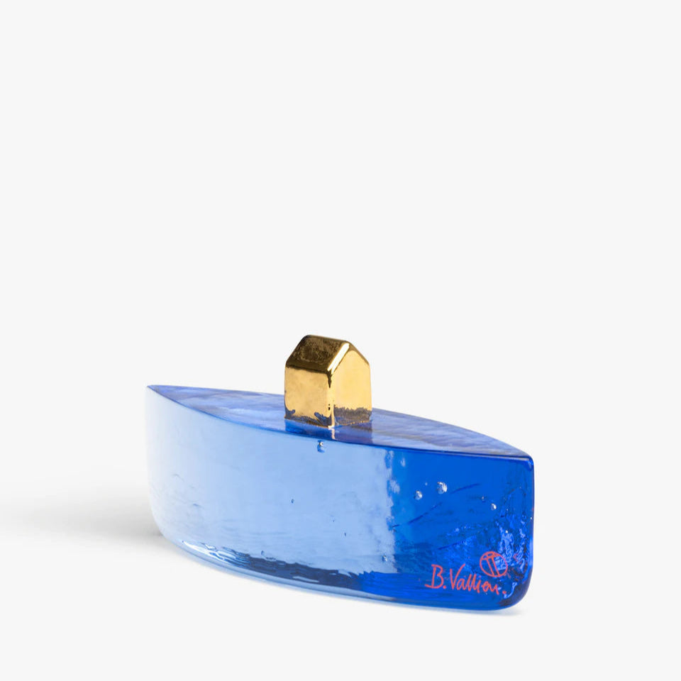 A blue glass sculpture with a gold-colored handle, part of the Fortress collection designed by Bertil Vallien for Kosta Boda, Sweden.