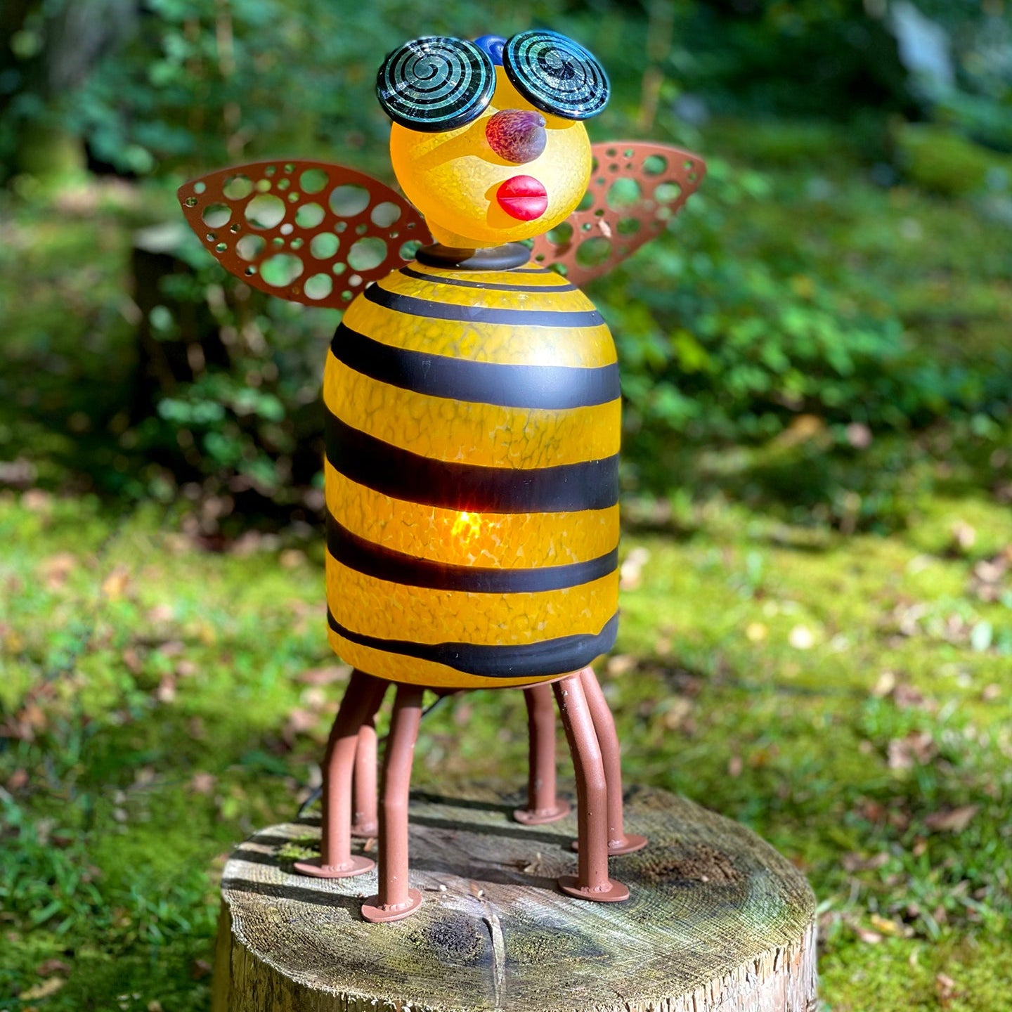 Colorful bee-shaped garden statue on a wooden stump with a blurred natural background