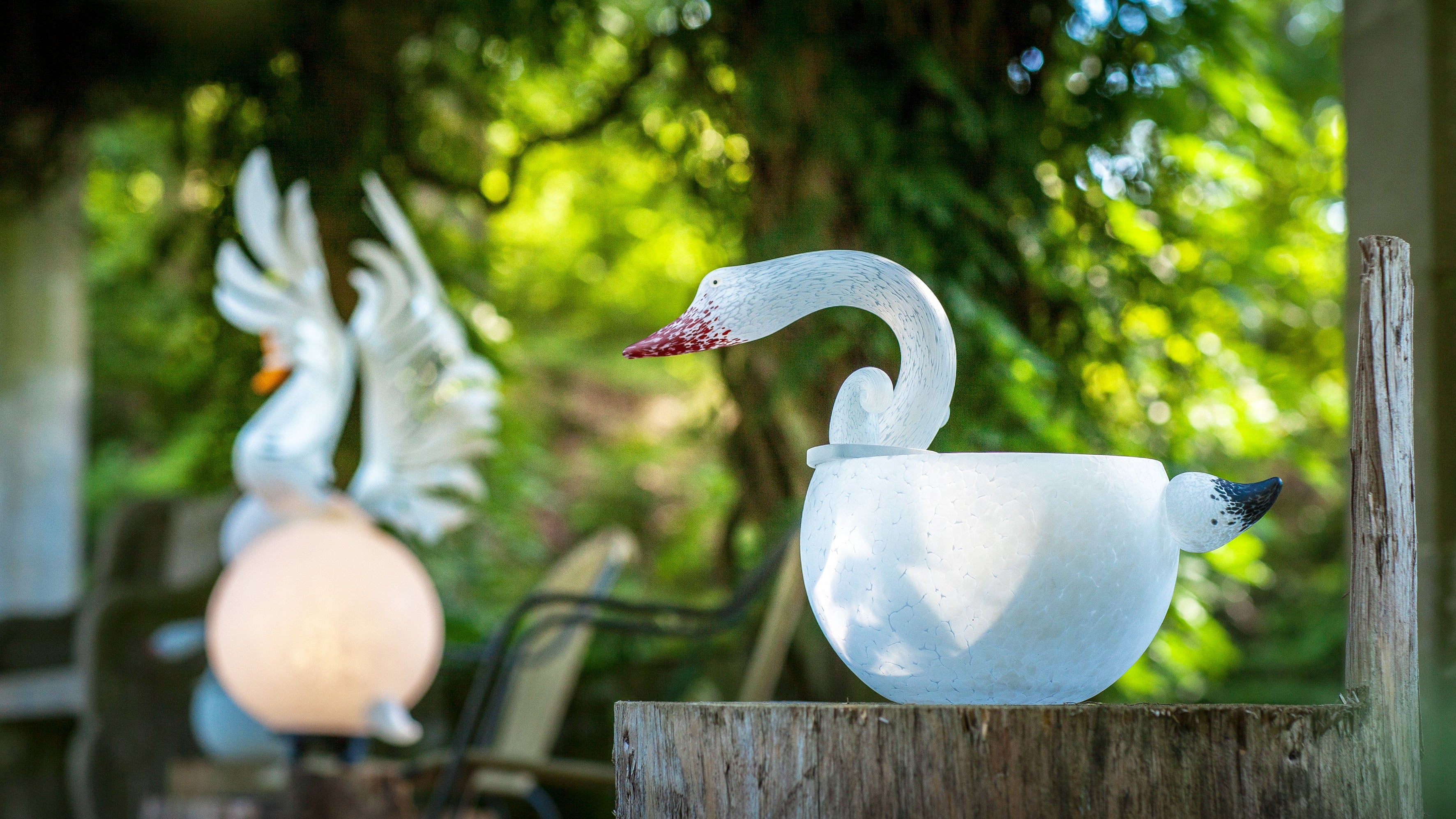 White swan-shaped outdoor light on a wooden post with blurred greenery in the background