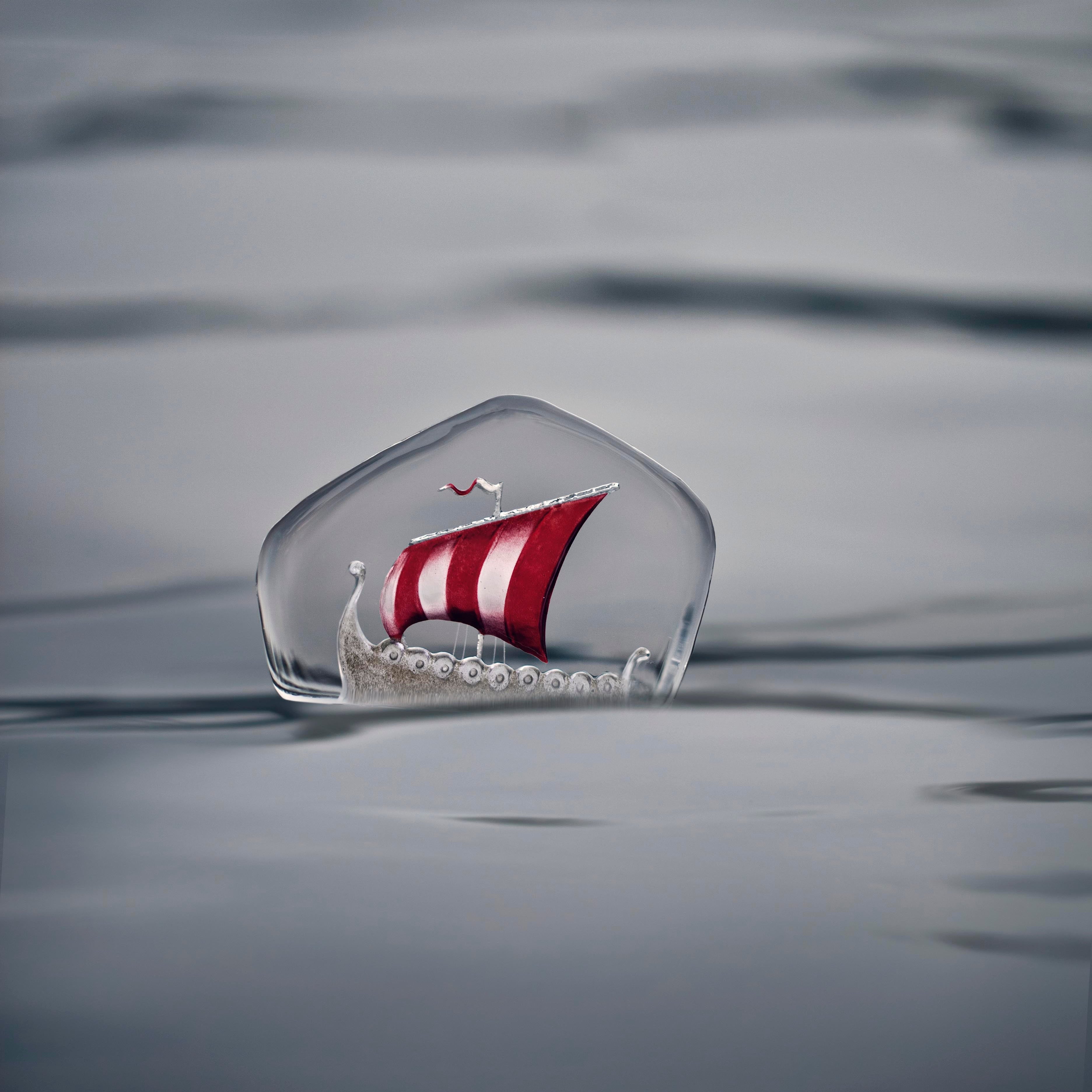 Glass sculpture of a sailboat with a red and white sail on a snowy background