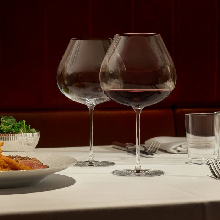 Frantzen Two wine glasses with red wine on a table with food and cutlery.