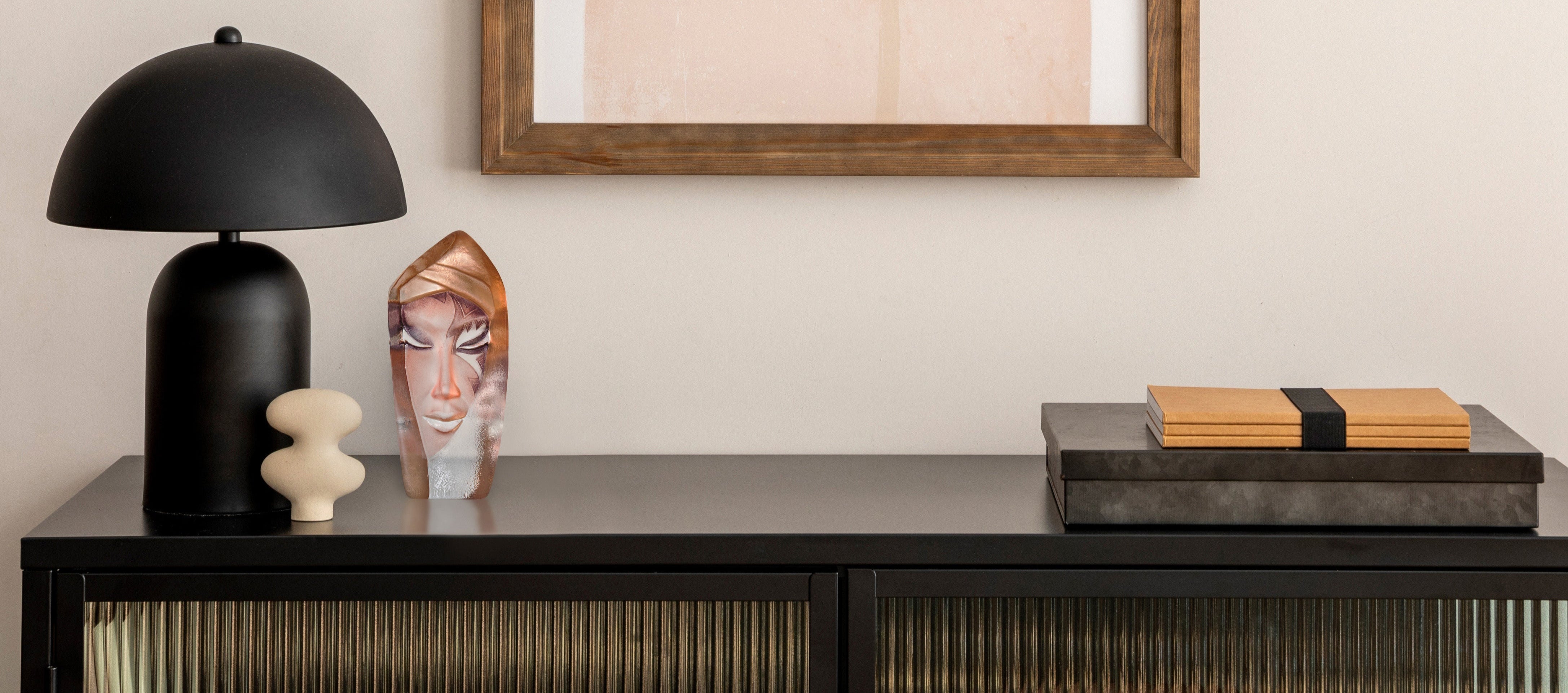 Modern head sculpture in glass with a black lamp, abstract art, and decorative items on a console table.