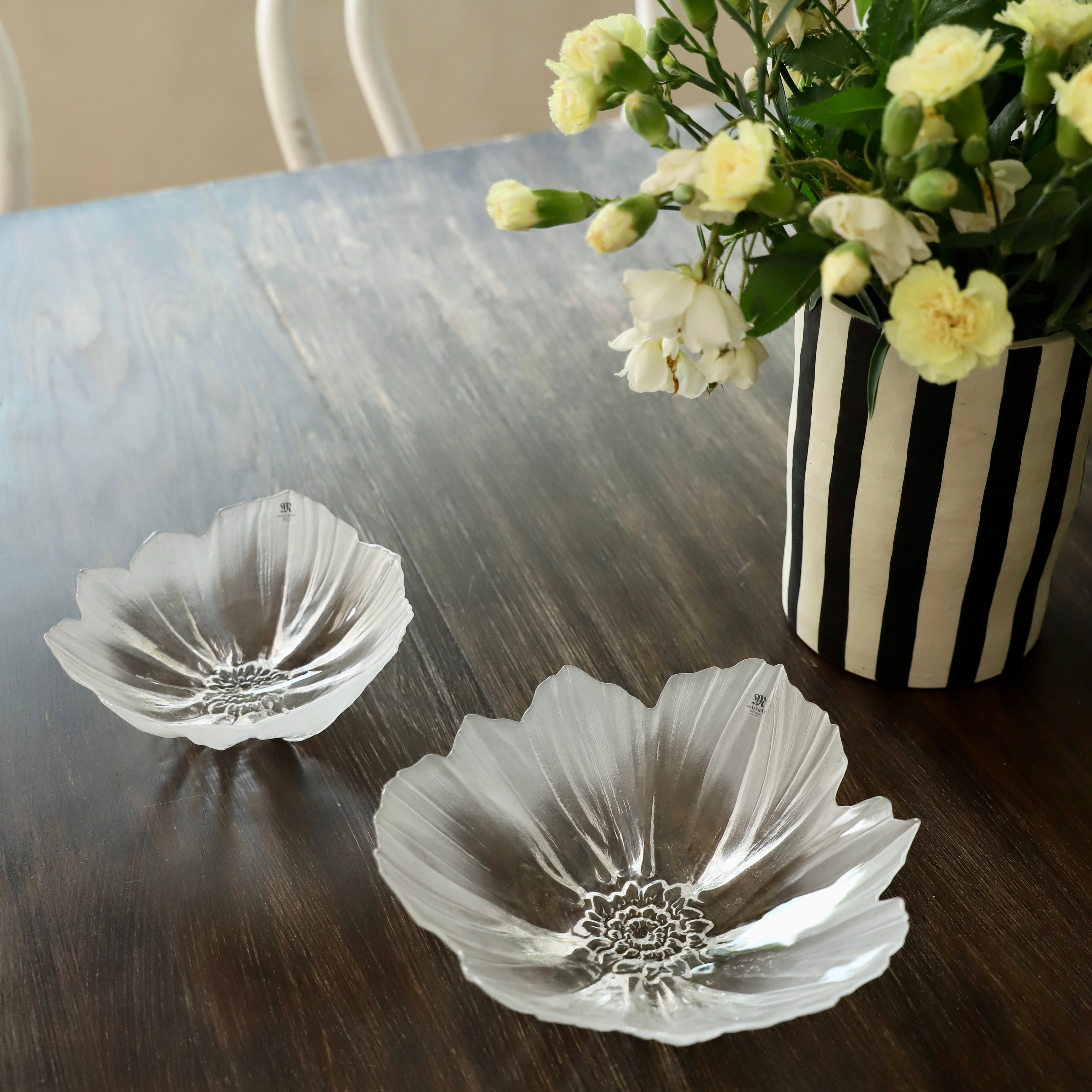 Maleras glass silver flower-shaped plates on a wooden table with a vase of flowers.