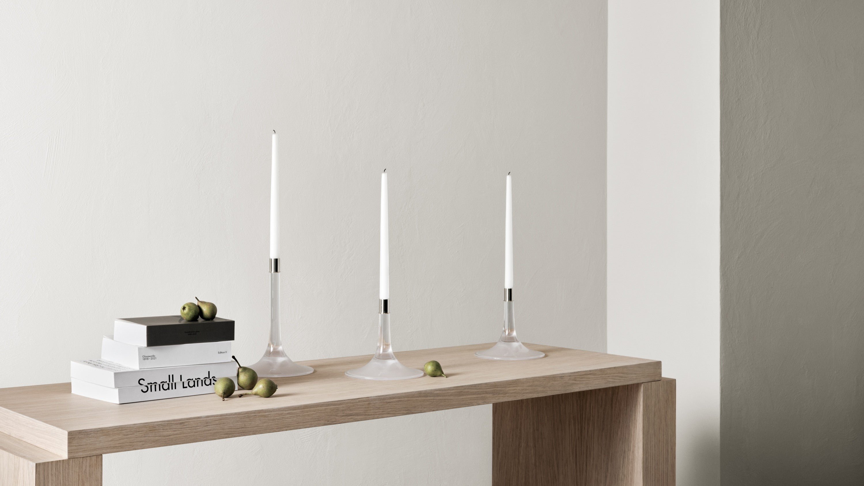 Orrefors Cirus candleholder inside interior with a wooden table, books, and decorative items against a plain wall.