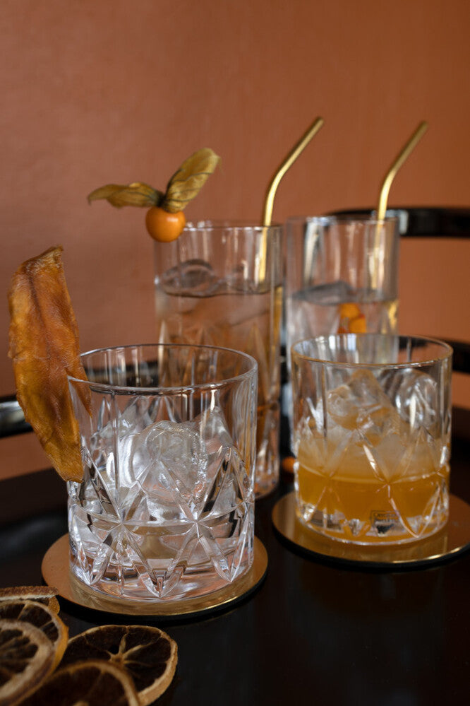 Cocktails with garnishes and straws on a dark surface with a warm background