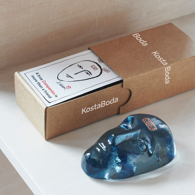 Kosta Boda Blue glass sculpture in front of a Kosta Boda box on a light wooden surface