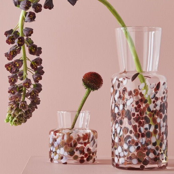 Two Kosta Boda Meadow glass vases with floral arrangements on a pink background