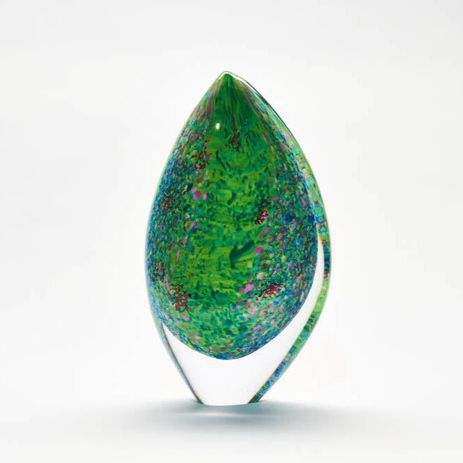 A tall, teardrop-shaped glass sculpture with green and blue colors, featuring a pattern of leaves and reeds with pink, lilac, and red accents.