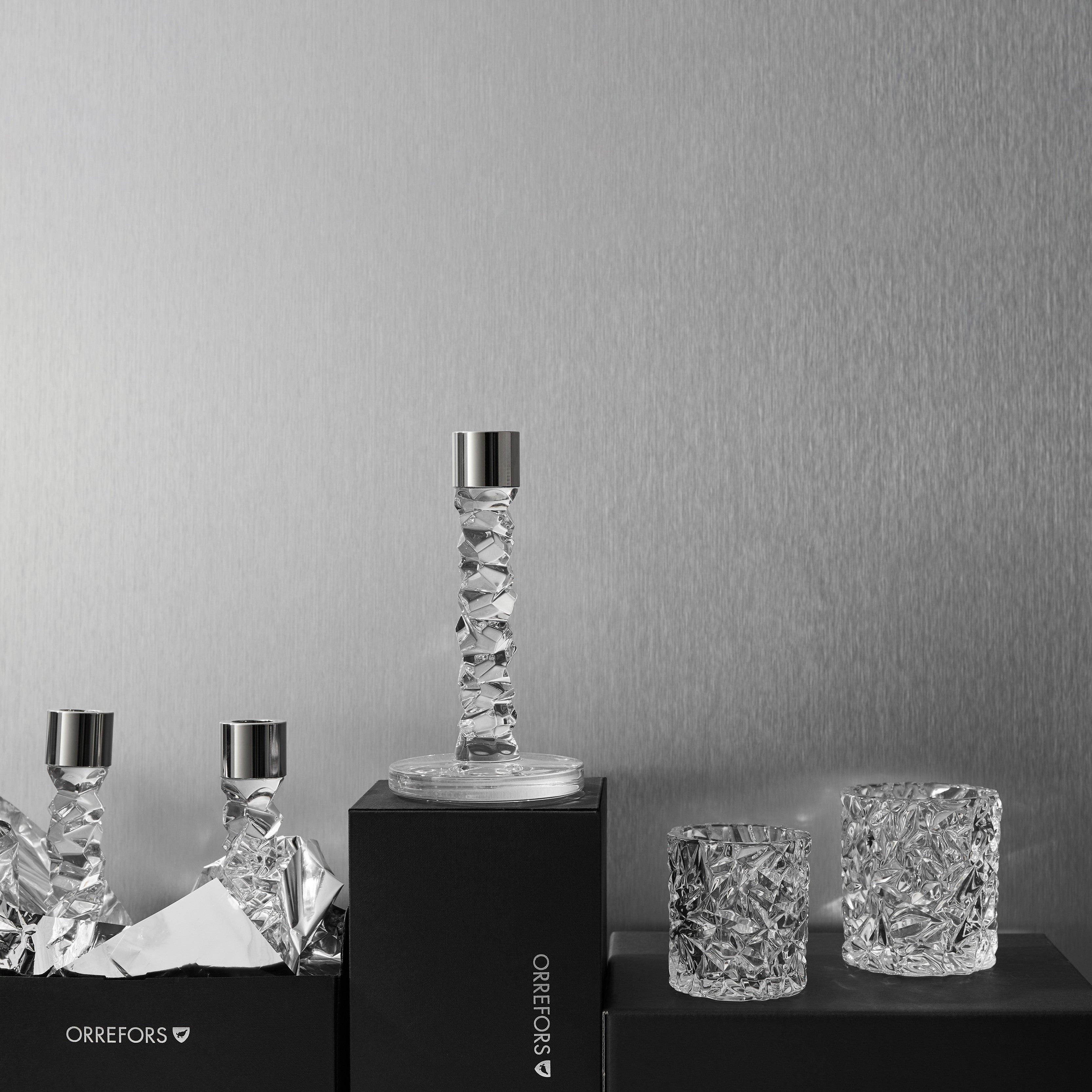Set of Orrefors Carat crystal candleholders and tea lights on black stands against a grey background