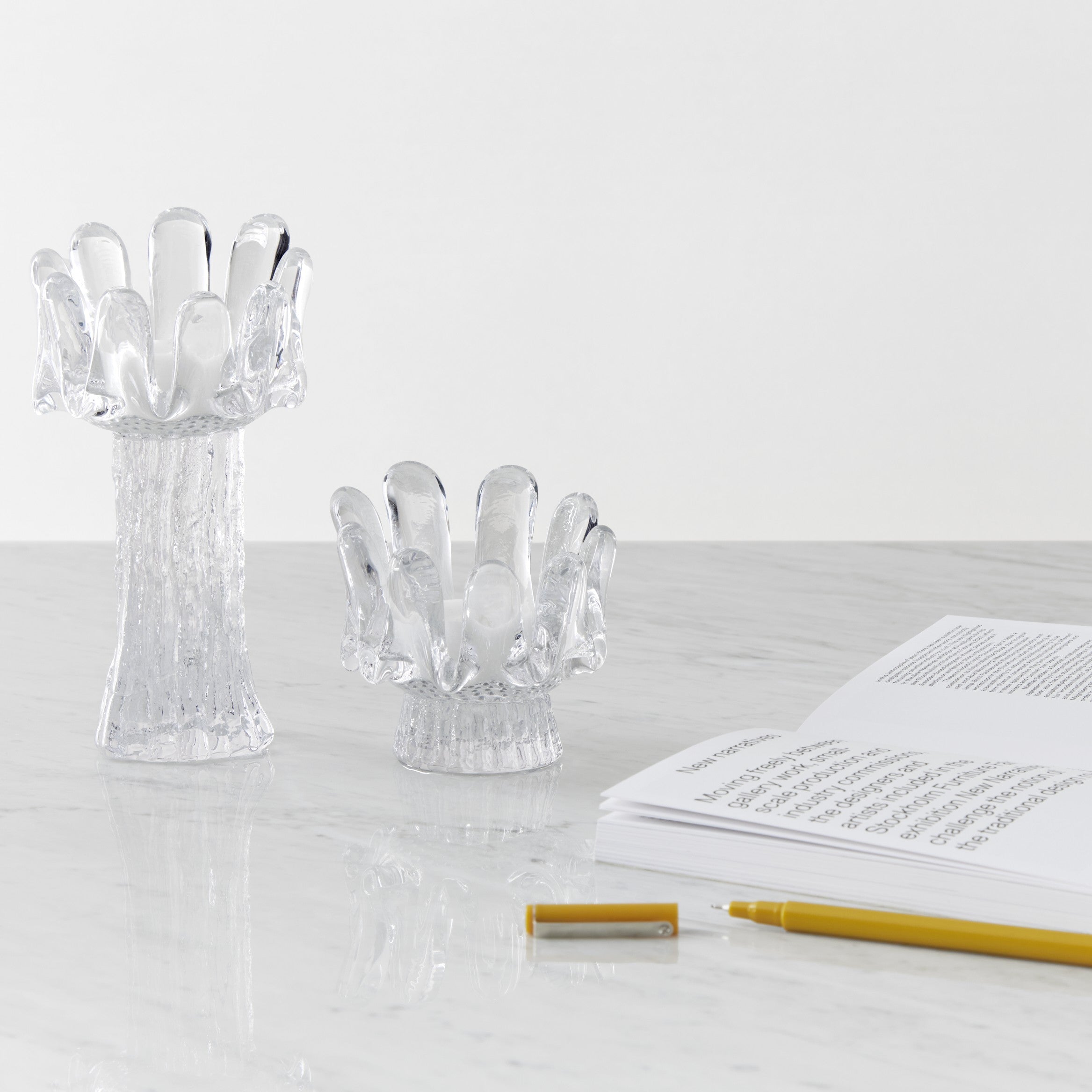 Clear glass hand-shaped candle holders on a white surface with an open book and yellow pen.