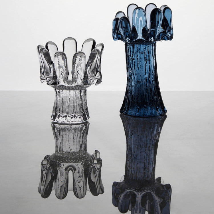 Two glass candle holders, one clear and one blue, on a reflective surface with a white background.