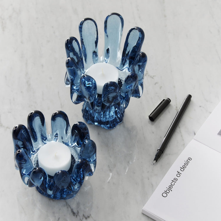 Two blue hand-shaped candle holders on a marble surface with a pen and book.