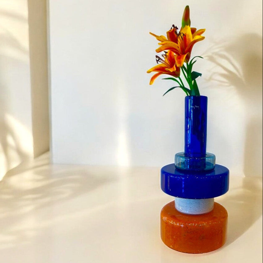 Blue and orange glass vase with flowers on a white surface with light shadows